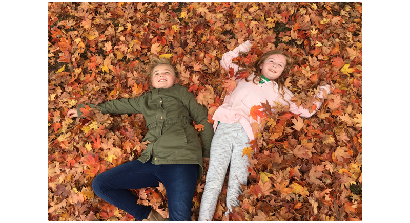 two young girls smiling and laying in fallen leaves
